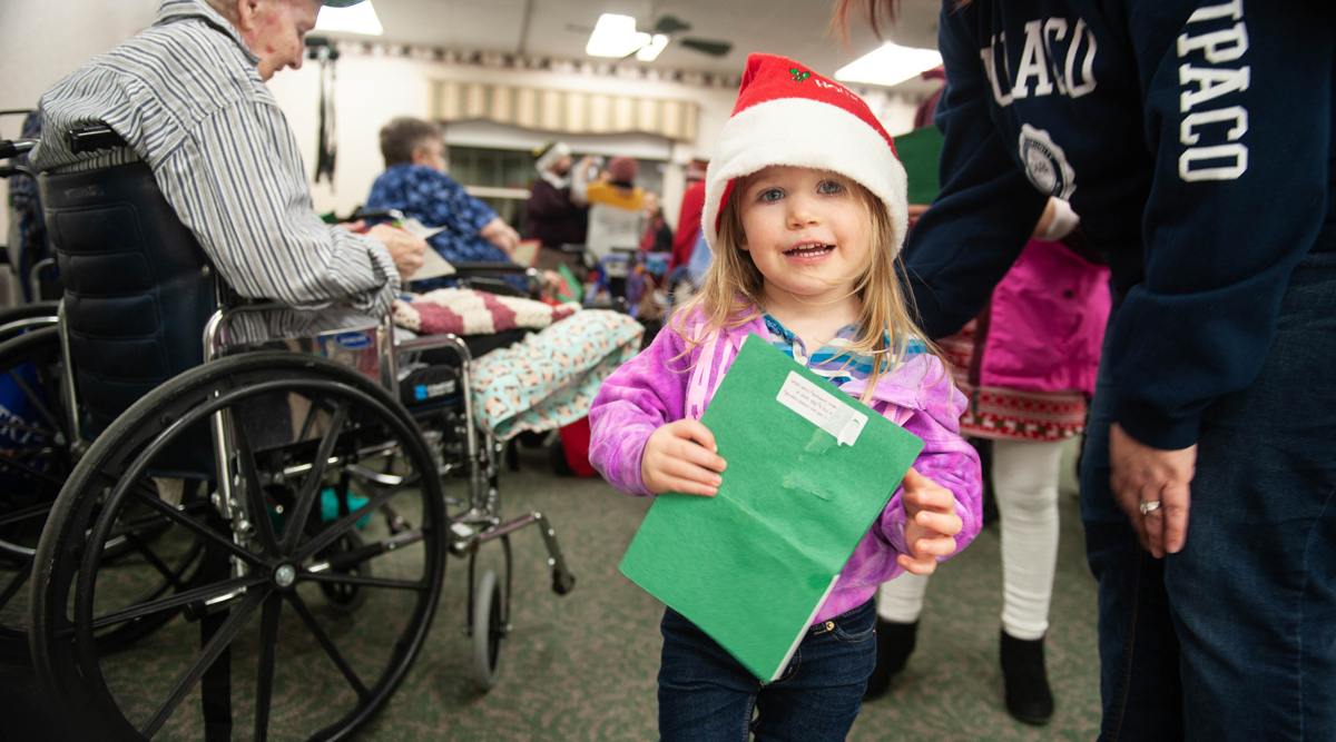 Dupaco's Kelly Houtakker's daughter, Carsyn, hands out homemade holiday cards while caroling at a local nursing home on Dec. 4, 2018 in Dubuque, Iowa. (M. Blondin/Dupaco photo)