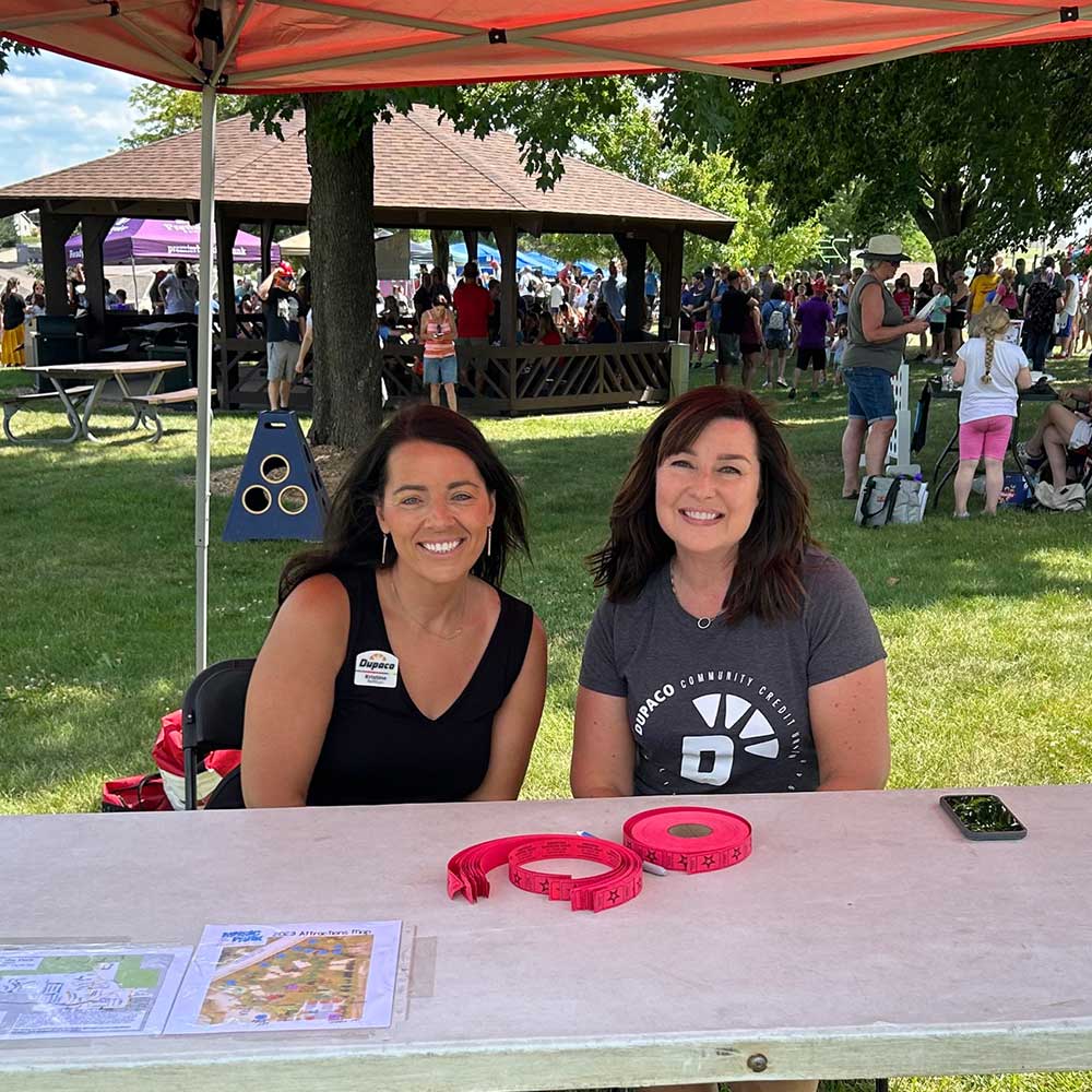 Dupaco employees under a tent outdoors on a sunny summer day issuing tickets to attendees at Music in the Park in Asbury, Iowa.