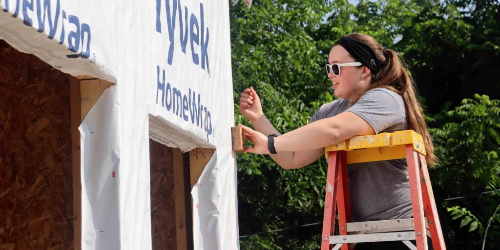 Cassie, a Dupaco team member, stands on a ladder near an open garage door, actively volunteering for Habitat for Humanity.