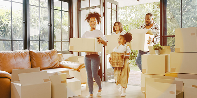 Four family members each carry a moving box in their living room