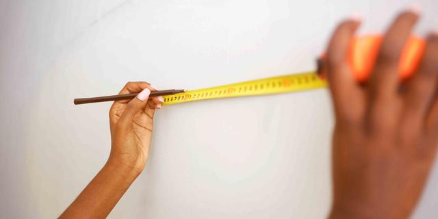 A pair of hands balances a tape measure against a wall